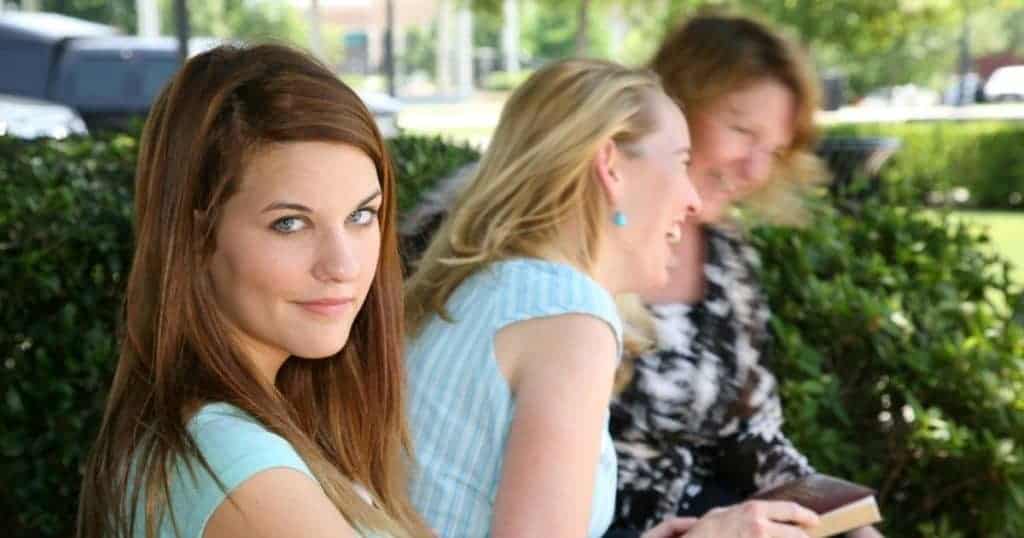 woman smiling while sitting on a bench with 2 other women 