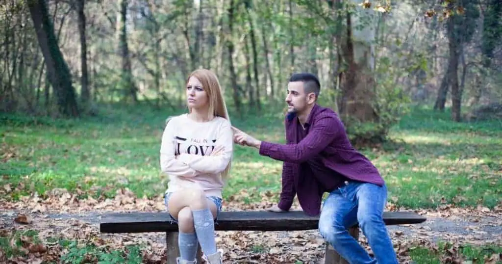 angry woman and apologizing man sitting on bench